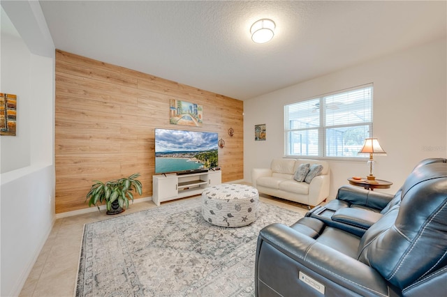 living area with an accent wall, wood walls, a textured ceiling, baseboards, and tile patterned floors