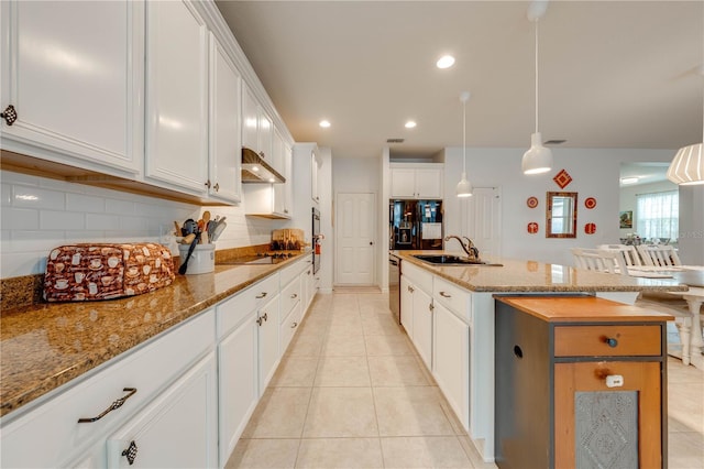 kitchen featuring tasteful backsplash, a kitchen island with sink, under cabinet range hood, a sink, and light tile patterned flooring