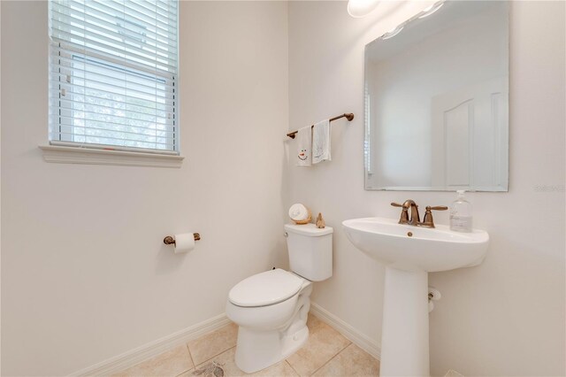 half bathroom with a sink, tile patterned flooring, toilet, and baseboards