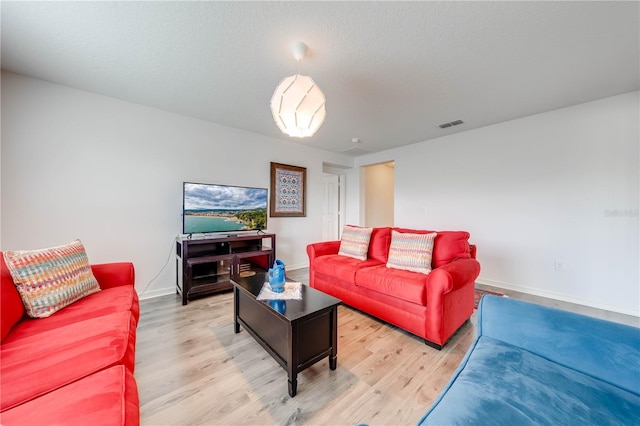 living area featuring visible vents, light wood-style flooring, baseboards, and a textured ceiling