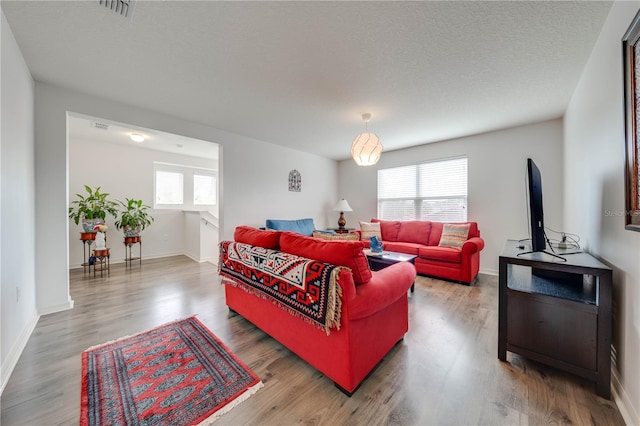 living area featuring baseboards, a textured ceiling, visible vents, and wood finished floors