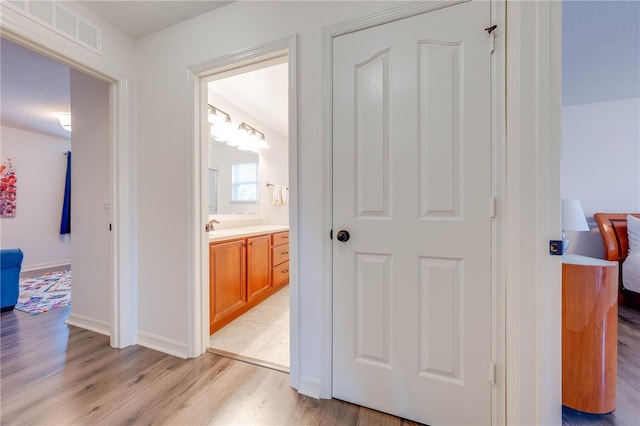 hallway featuring light wood-style floors, baseboards, and visible vents