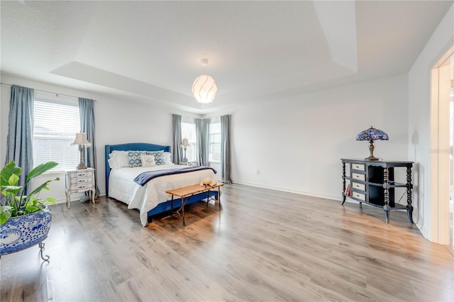 bedroom featuring a tray ceiling, multiple windows, and light wood-style floors