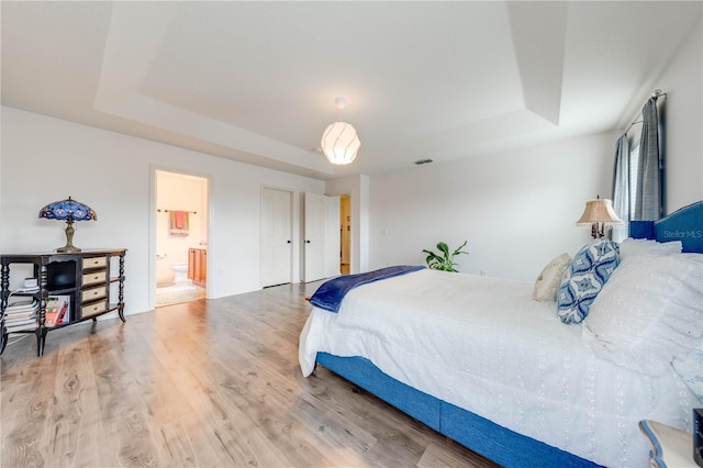 bedroom with ensuite bath, a raised ceiling, and wood finished floors