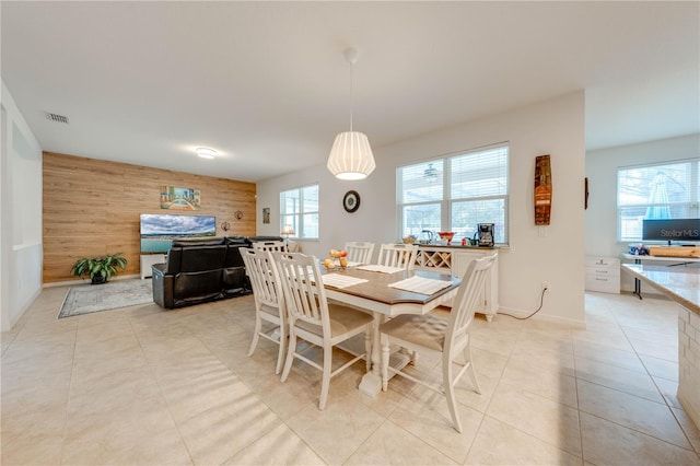 dining space with light tile patterned floors, wooden walls, baseboards, visible vents, and an accent wall