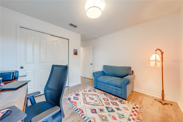 home office with visible vents, a textured ceiling, baseboards, and wood finished floors