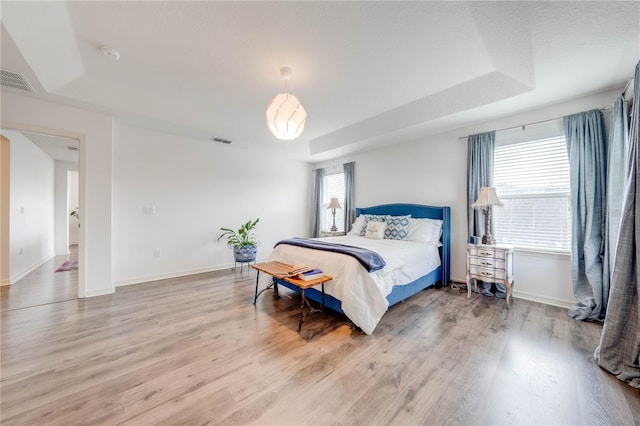 bedroom with a tray ceiling, visible vents, light wood-style flooring, and baseboards