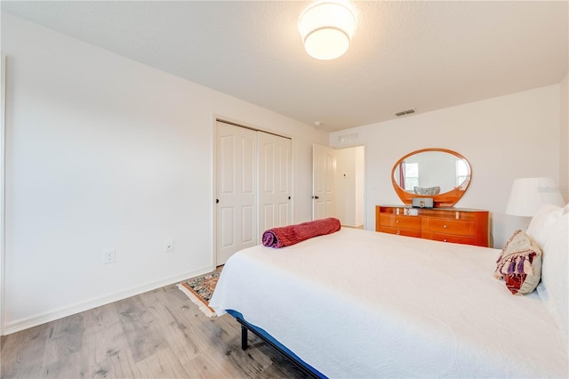 bedroom with a textured ceiling, wood finished floors, visible vents, baseboards, and a closet