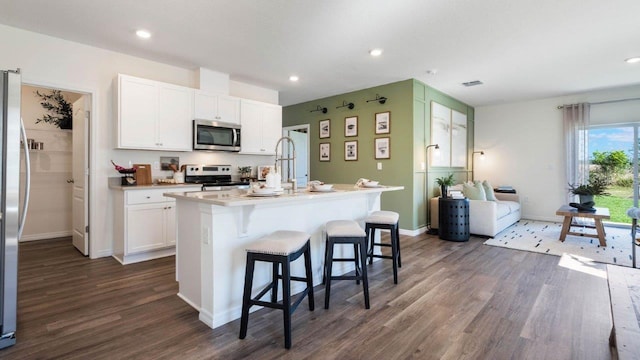 kitchen with appliances with stainless steel finishes, a kitchen island with sink, light countertops, a kitchen bar, and white cabinetry