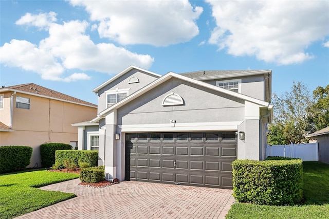 traditional-style house featuring decorative driveway, fence, an attached garage, and stucco siding