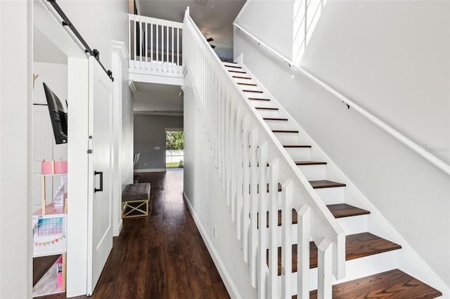 staircase featuring a towering ceiling, a barn door, baseboards, and wood finished floors