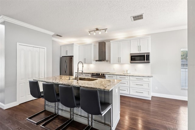 kitchen with stainless steel appliances, a kitchen island with sink, wall chimney exhaust hood, and white cabinetry