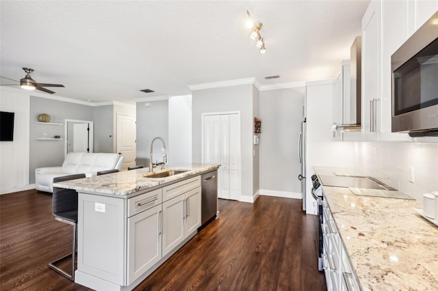 kitchen featuring a sink, white cabinetry, open floor plan, appliances with stainless steel finishes, and a center island with sink