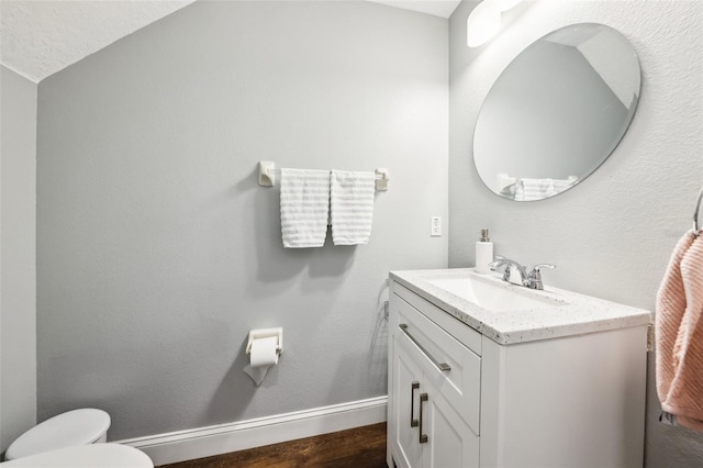 half bath with toilet, wood finished floors, vanity, and baseboards