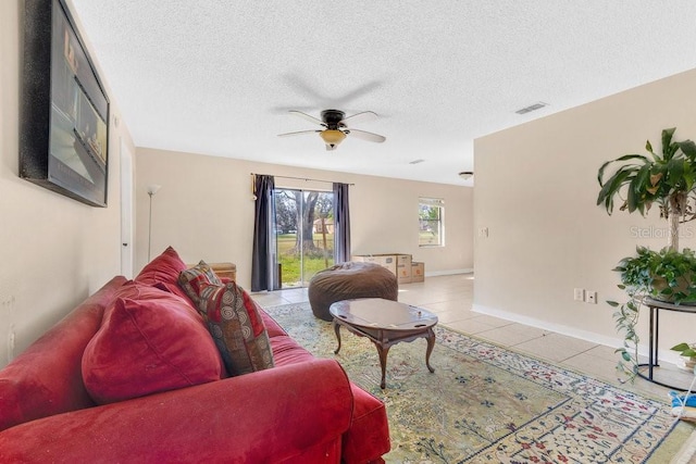 living area featuring light tile patterned floors, a textured ceiling, visible vents, a ceiling fan, and baseboards