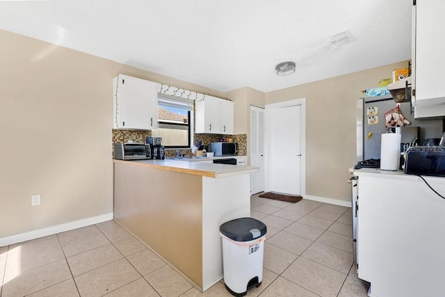 kitchen featuring light tile patterned floors, tasteful backsplash, light countertops, white cabinets, and a peninsula