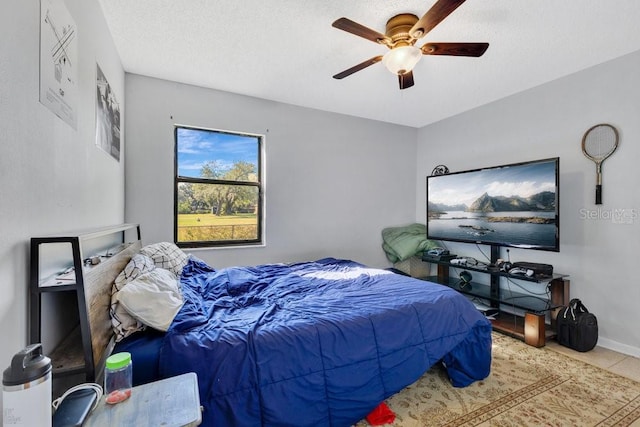 bedroom with tile patterned flooring, ceiling fan, a textured ceiling, and baseboards