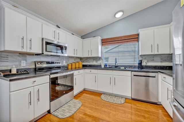 kitchen with dark countertops, appliances with stainless steel finishes, vaulted ceiling, light wood-type flooring, and a sink