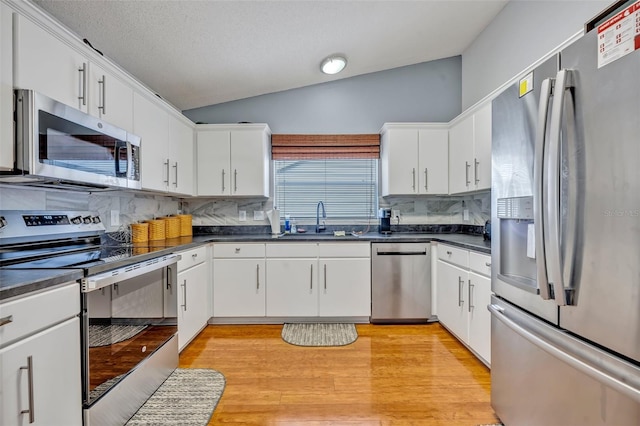 kitchen with dark countertops, appliances with stainless steel finishes, vaulted ceiling, and a sink