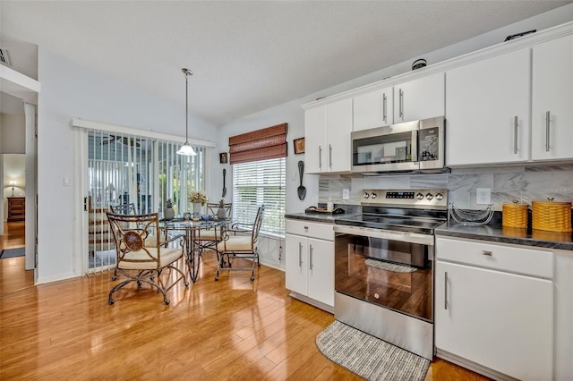 kitchen with dark countertops, appliances with stainless steel finishes, white cabinets, vaulted ceiling, and light wood-type flooring