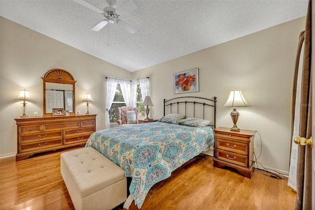 bedroom with a textured ceiling, wood finished floors, a ceiling fan, baseboards, and vaulted ceiling