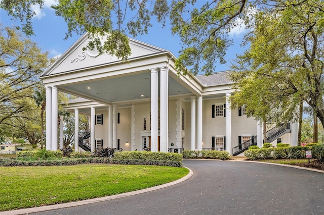 greek revival inspired property featuring aphalt driveway, stairs, a front lawn, and stucco siding