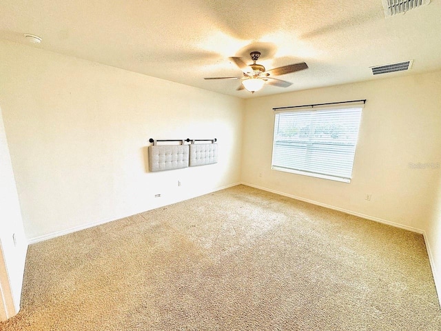 carpeted empty room with a ceiling fan, visible vents, a textured ceiling, and baseboards