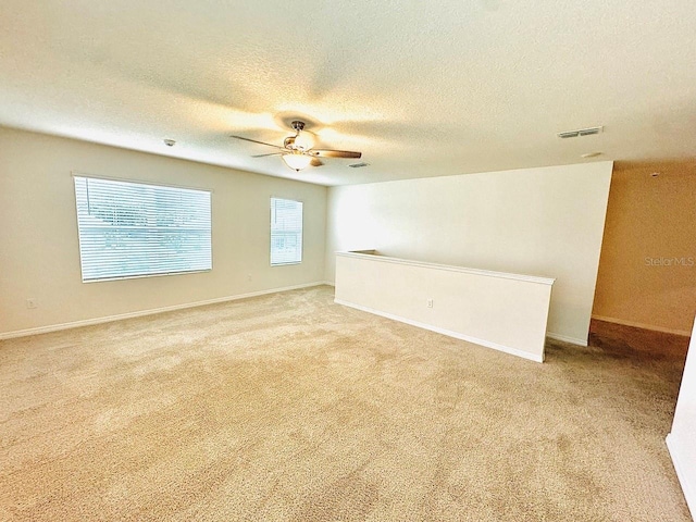 carpeted spare room featuring ceiling fan, a textured ceiling, visible vents, and baseboards