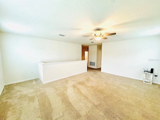 carpeted spare room with baseboards, ceiling fan, visible vents, and a textured ceiling