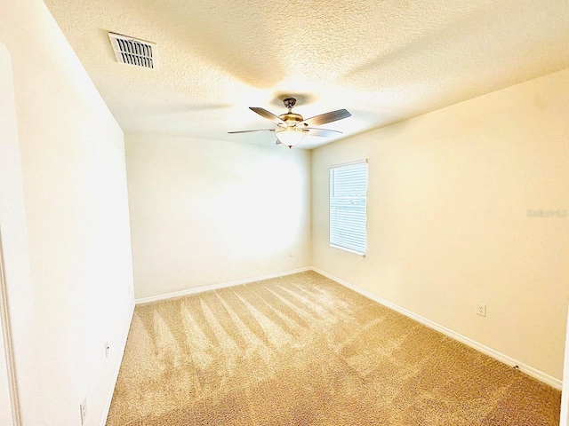 carpeted empty room featuring baseboards, a textured ceiling, visible vents, and a ceiling fan