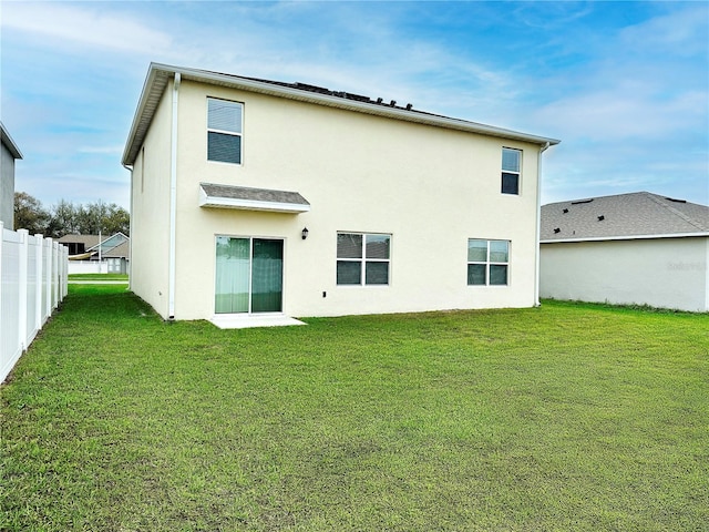 rear view of house featuring stucco siding, fence, and a lawn