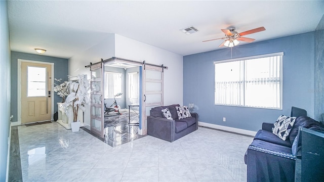 living area with a barn door, light tile patterned flooring, a ceiling fan, visible vents, and baseboards