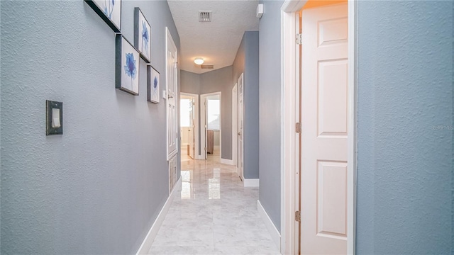 hallway featuring visible vents, a textured wall, a textured ceiling, and baseboards