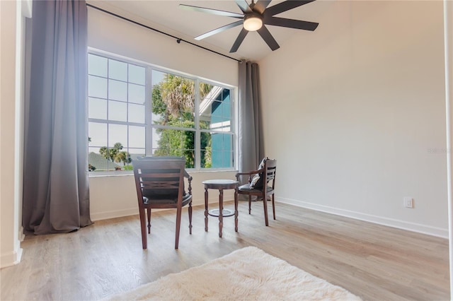 living area with light wood finished floors, a ceiling fan, and baseboards