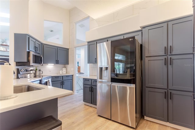 kitchen featuring stainless steel appliances, light countertops, gray cabinetry, light wood-style floors, and backsplash