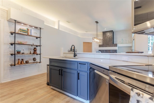 kitchen with decorative light fixtures, light countertops, appliances with stainless steel finishes, a sink, and light wood-type flooring