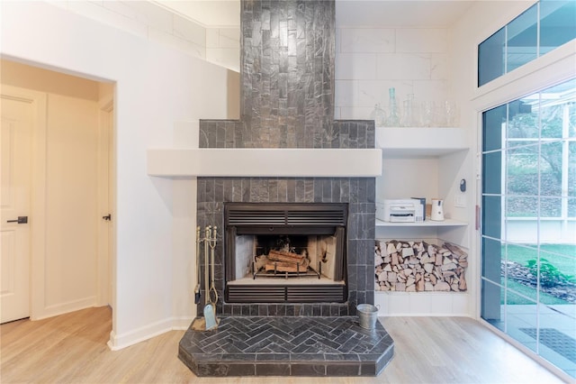 interior details with a tiled fireplace, baseboards, and wood finished floors