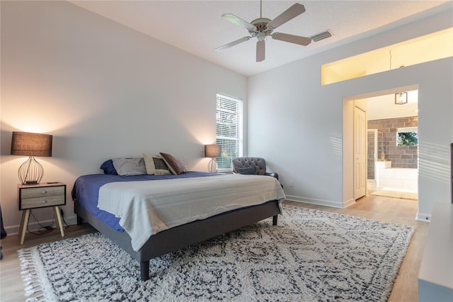 bedroom featuring baseboards, visible vents, ensuite bath, wood finished floors, and vaulted ceiling