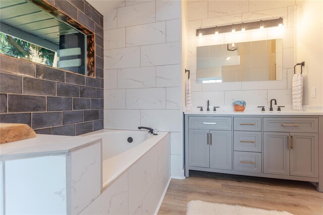 bathroom featuring tile walls, double vanity, a bathing tub, a sink, and wood finished floors