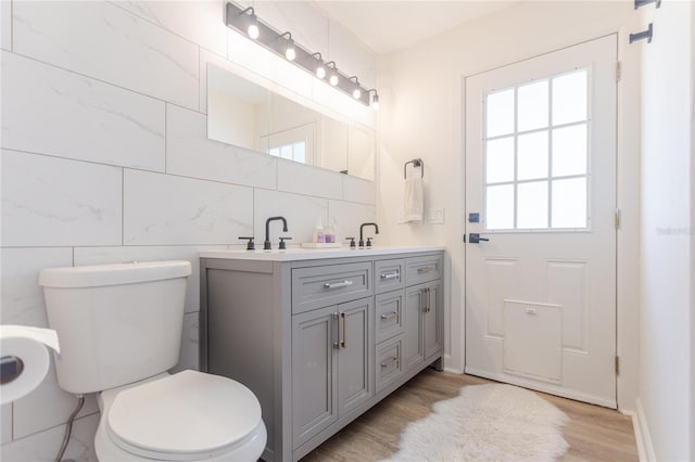 bathroom with tile walls, double vanity, tasteful backsplash, toilet, and wood finished floors