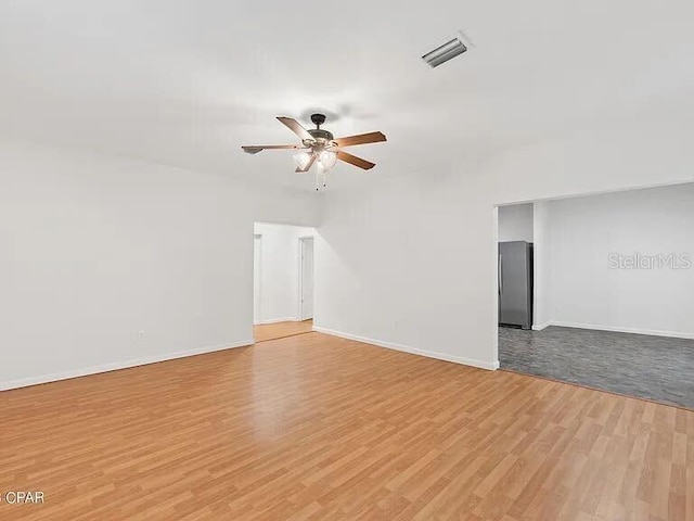 spare room with light wood finished floors, baseboards, visible vents, and a ceiling fan