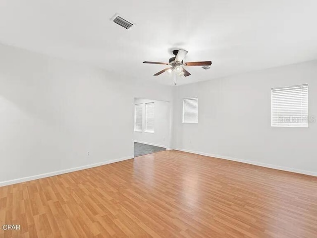 empty room with light wood-style flooring, a ceiling fan, visible vents, and baseboards