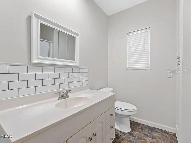 bathroom featuring toilet, vanity, baseboards, backsplash, and stone finish floor