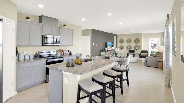 kitchen featuring a center island with sink, appliances with stainless steel finishes, light stone counters, and gray cabinetry