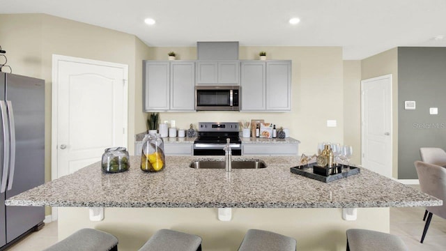 kitchen featuring stainless steel appliances, an island with sink, light stone countertops, and gray cabinetry