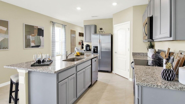 kitchen with stainless steel appliances, a kitchen island with sink, a sink, and gray cabinetry