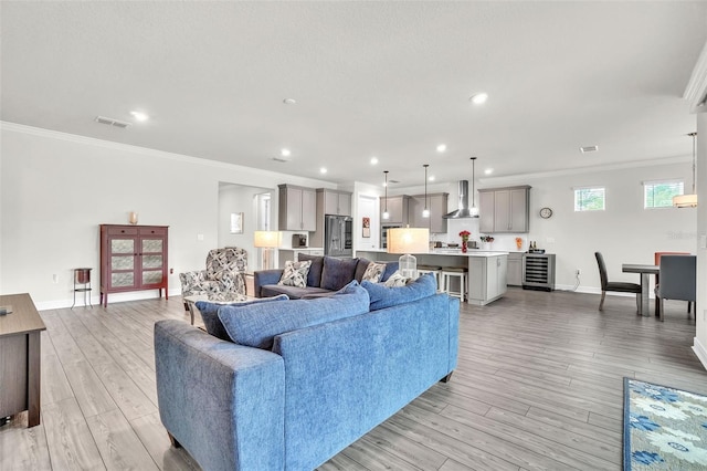 living room featuring light wood-style floors, beverage cooler, crown molding, and baseboards