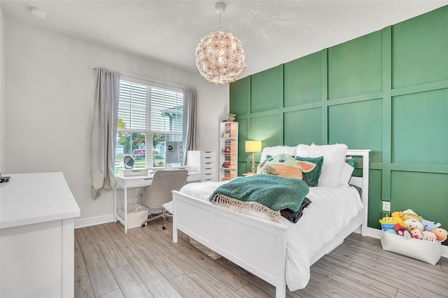 bedroom featuring light wood-style floors, baseboards, a decorative wall, and an inviting chandelier