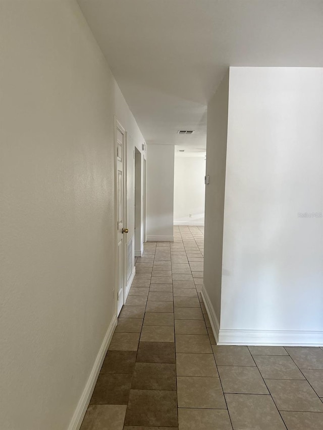 hallway with baseboards, visible vents, and dark tile patterned flooring