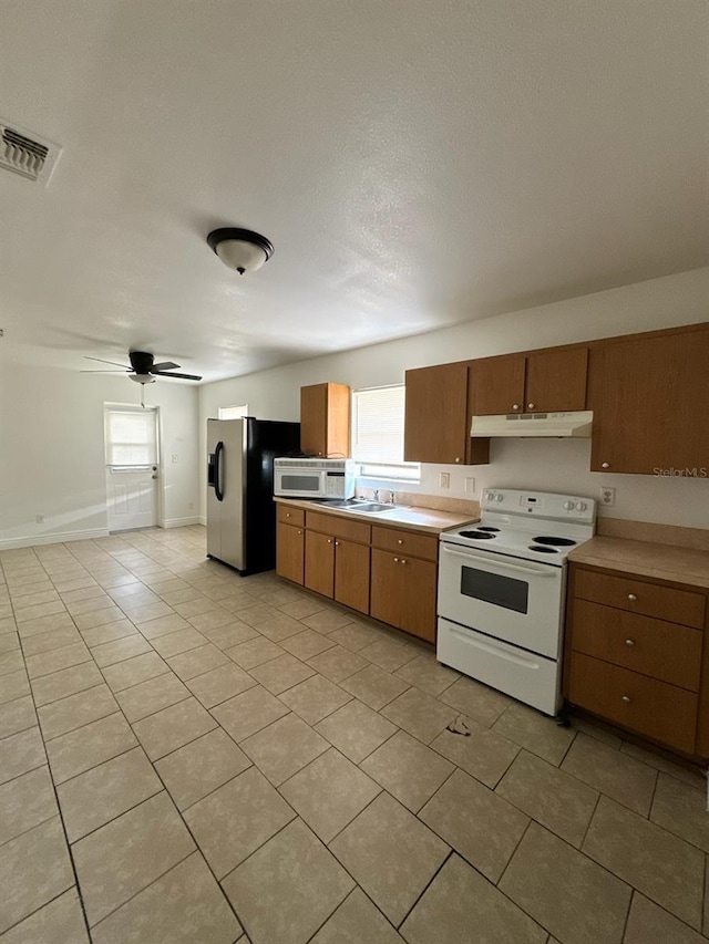 kitchen with under cabinet range hood, white appliances, light countertops, brown cabinets, and plenty of natural light